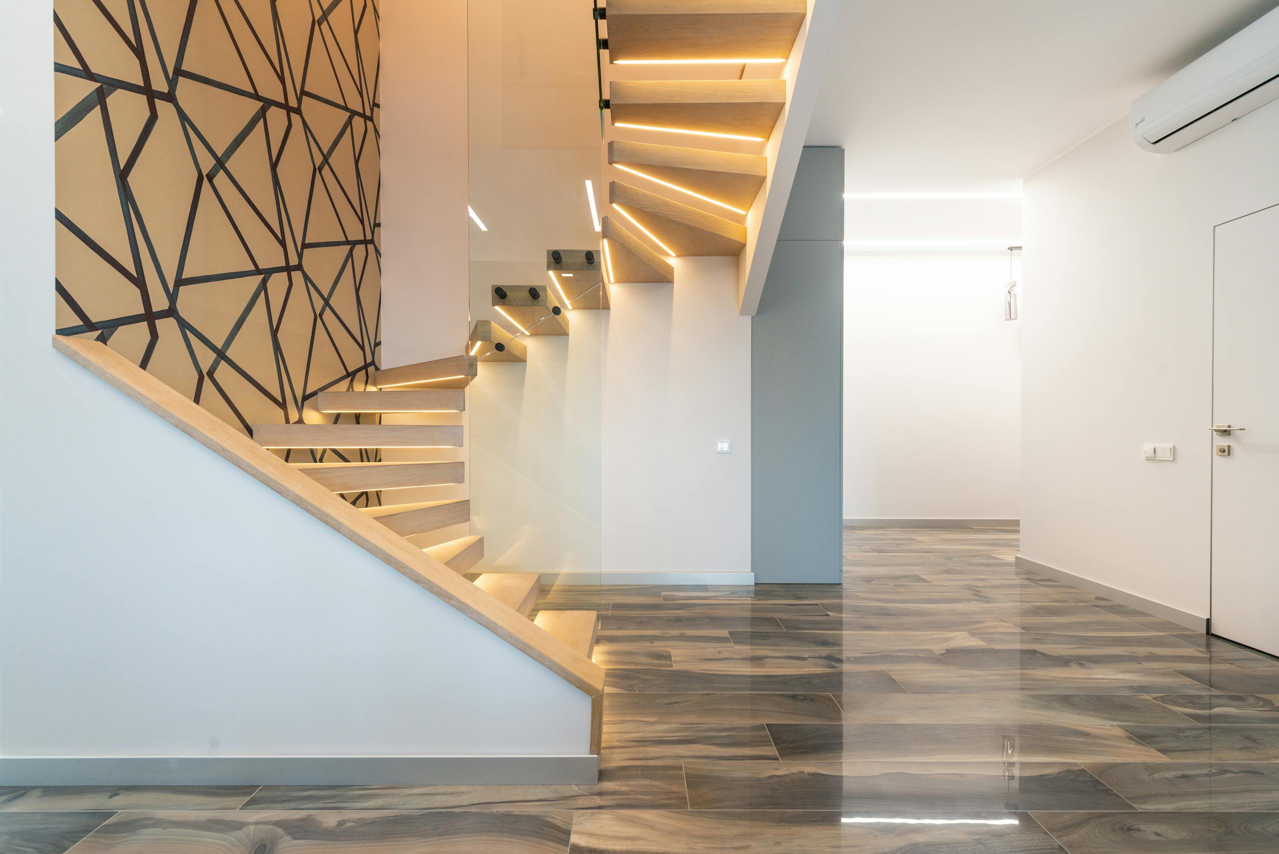 Contemporary hall interior with door against curved staircase and wall with geometric ornament in light house